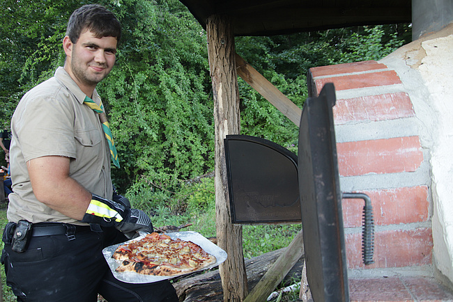 Die Pizza ist fertig - stolz präsentiert ein Pfadfinder das Ergebnis