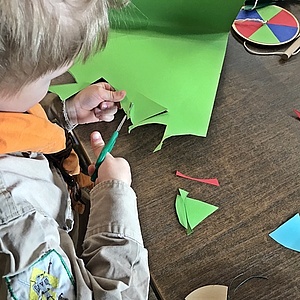 Ein Kind schneidet aus grünem Tonkarton Farbschnipsel aus