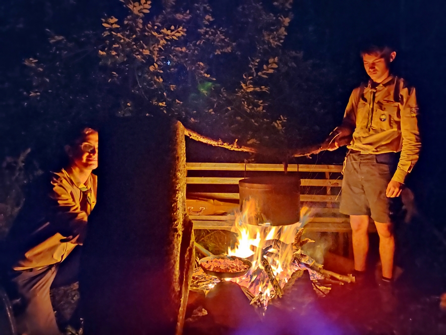 Zwei Pfadfinder kochen Essen in einem Topf über dem Lagerfeuer